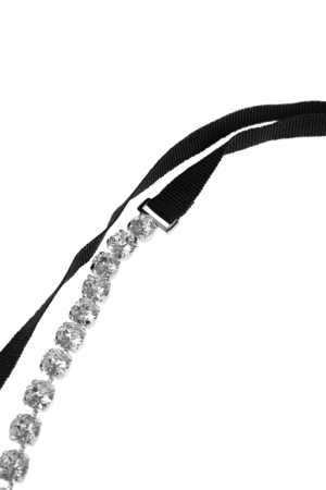 Close-up of a diamond tennis necklace laid along a black ribbon on a white background.