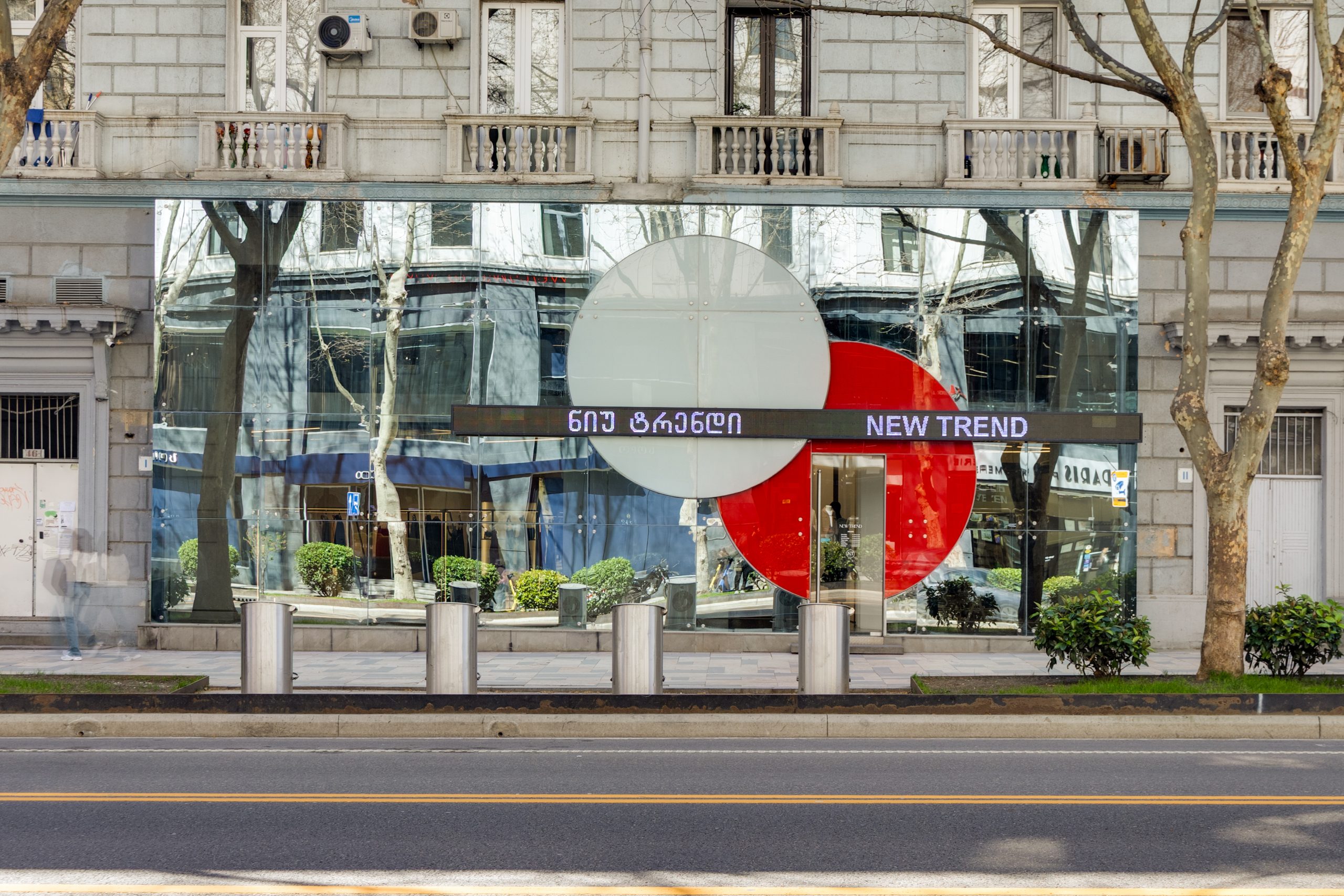 Storefront with large reflective glass windows showing street reflections, a large circular red and gray design, and a 'NEW TREND' sign across the entrance area.