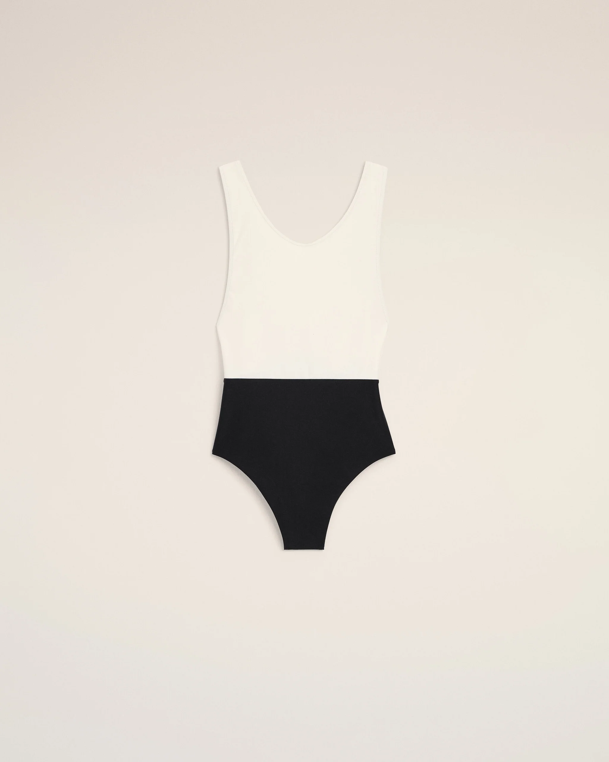 Flat lay of a white sleeveless top paired with a black high-waisted bottom on a pale beige background, forming a color-block swimsuit silhouette.