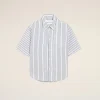 White button-down shirt with blue vertical stripes displayed against a pale beige background, centered in the frame.