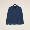 Blue long-sleeve shirt with white stitching on a beige backdrop; small heart emblem near the hem.