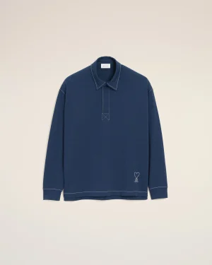 Blue long-sleeve shirt with white stitching on a beige backdrop; small heart emblem near the hem.