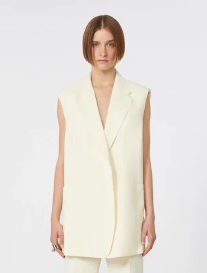 Model wearing a cream sleeveless blazer with wide shoulders and long length over matching pants.