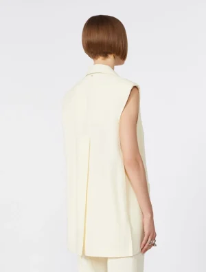 Back view of a person wearing a sleeveless cream-colored blazer-like vest over matching pants, short brown bob hairstyle, plain white background.
