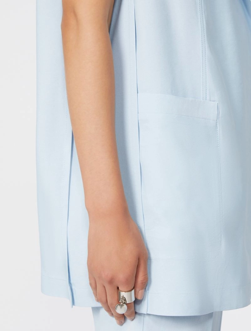 Close-up of a light blue coat sleeve with a front pocket and a hand wearing a silver ring.