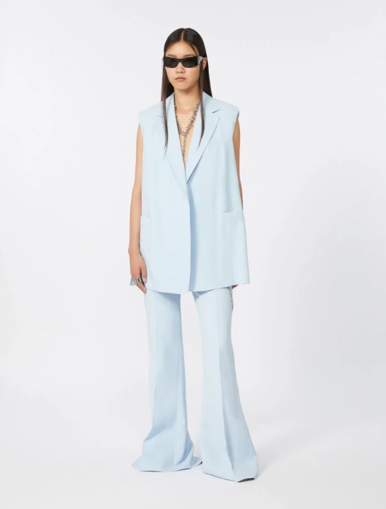 Model wearing a light blue sleeveless blazer and matching wide-leg pants with sunglasses.",