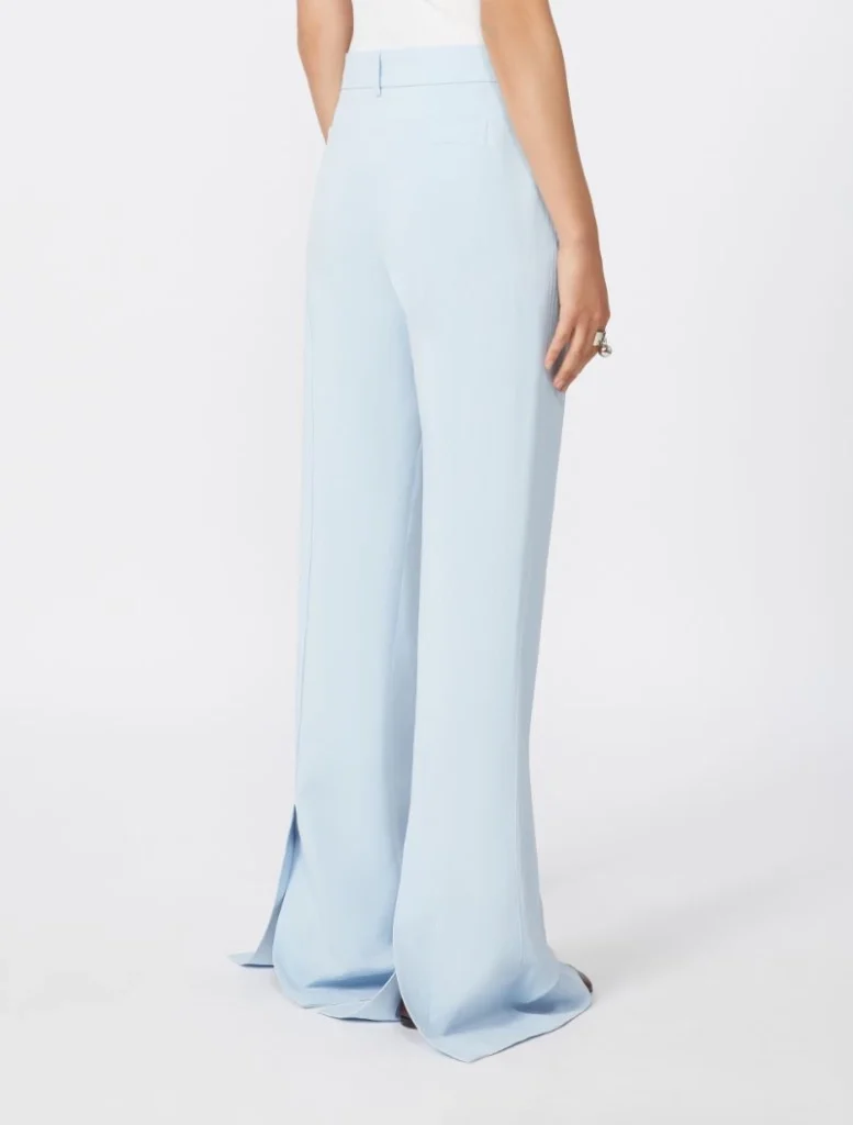 Back view of a person wearing light blue wide-leg trousers that puddle slightly at the floor, showing a tailored high waist and belt loops.