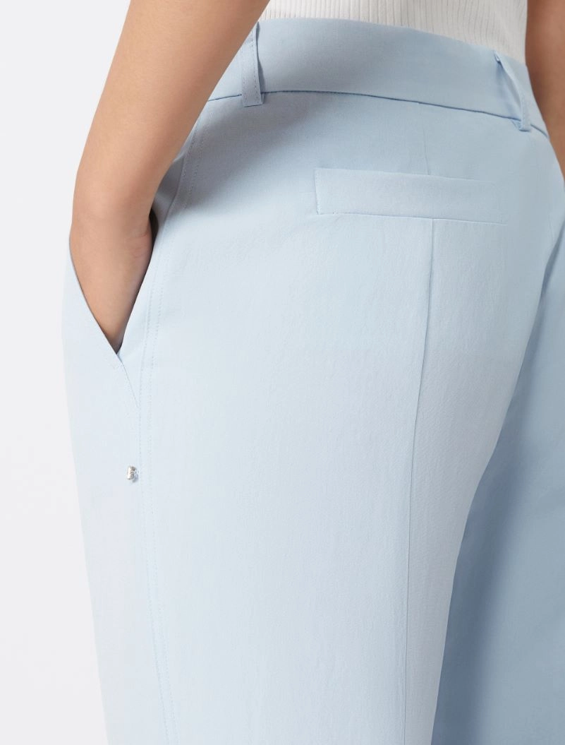 Close-up of light blue dress pants with a back welt pocket and a hand in the side pocket on the hip area.