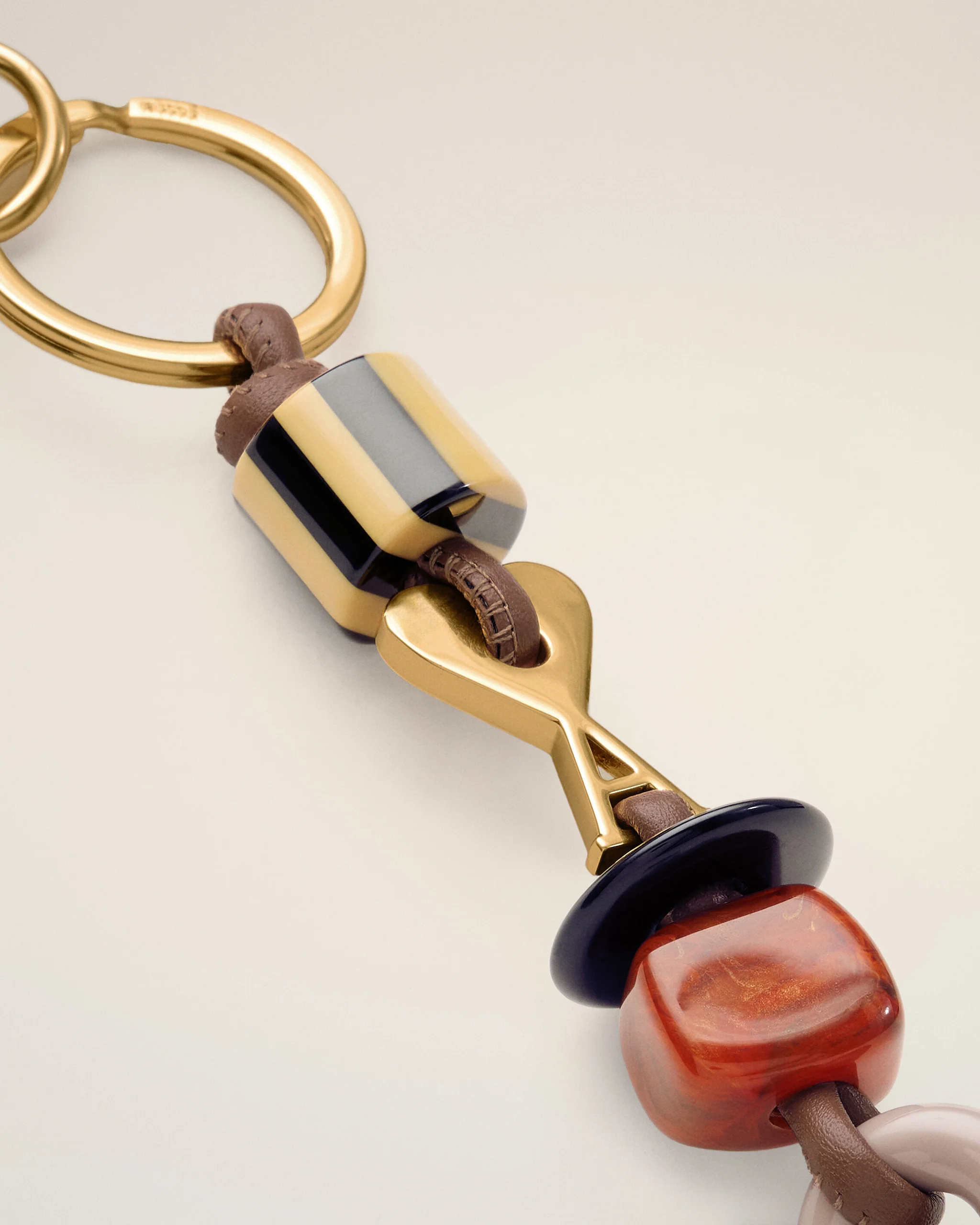 Close-up of a gold-tone bracelet with a brown leather strand and a striped bead (black, beige, gray).