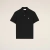 Black polo shirt with a small white heart emblem on the left chest against a beige background.