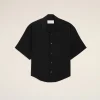 Flat lay of a black short-sleeve button-down shirt on a beige background, tag visible at the collar