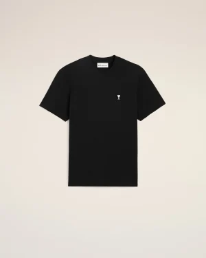 Black short-sleeve T-shirt with a small white heart-and-letter logo on the chest against a beige backdrop.