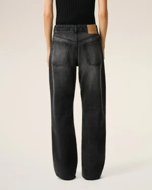 Back view of a person wearing dark, washed denim jeans with large back pockets and a tan leather patch on the waistband progressively visible on the right side.
