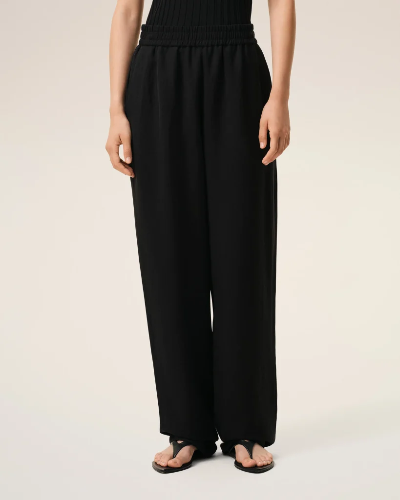Front view of person wearing black wide-leg pants with an elastic waistband, standing barefoot in sandals.