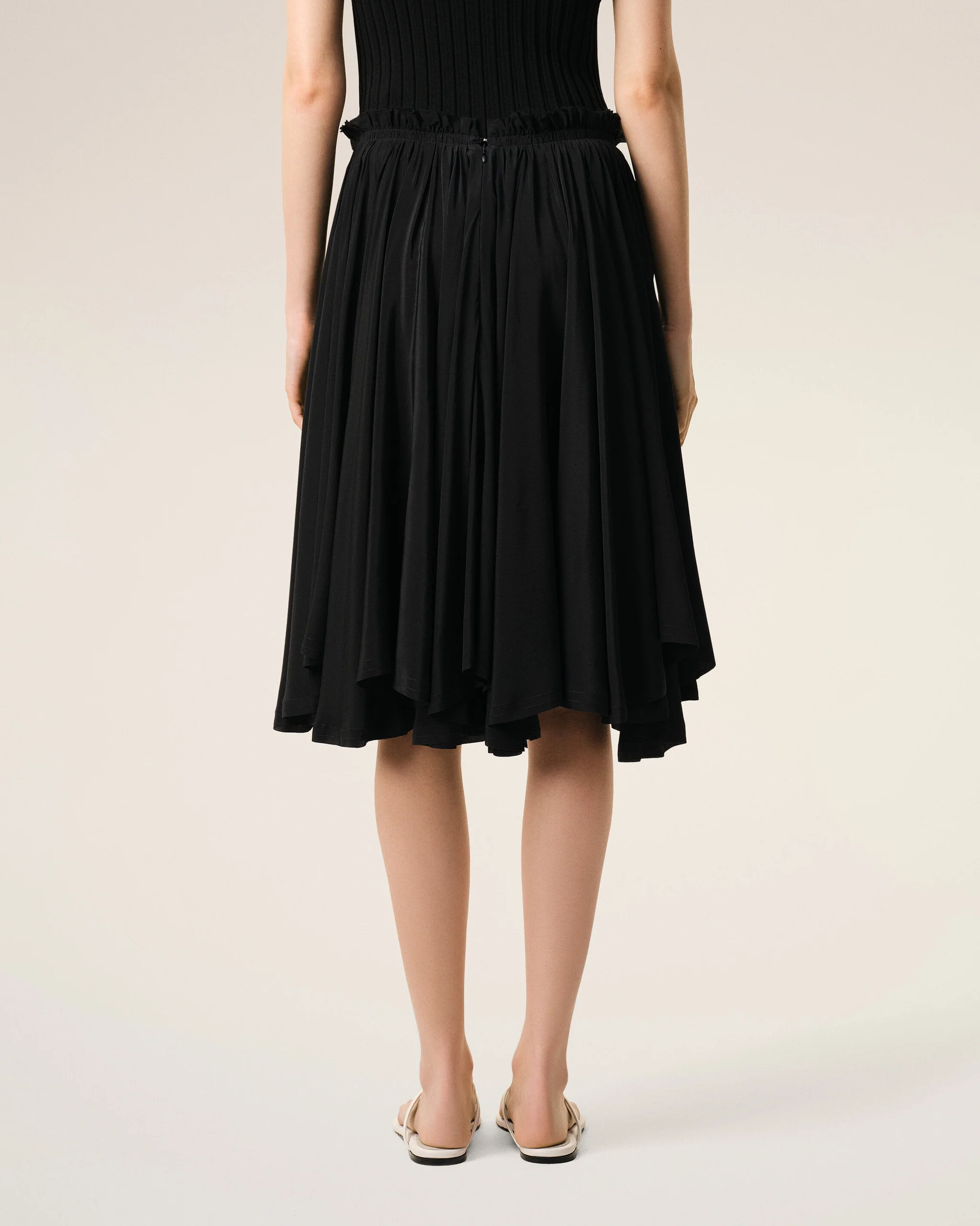 Back view of a person wearing a black dress with a ruched waistband and flat sandals.
