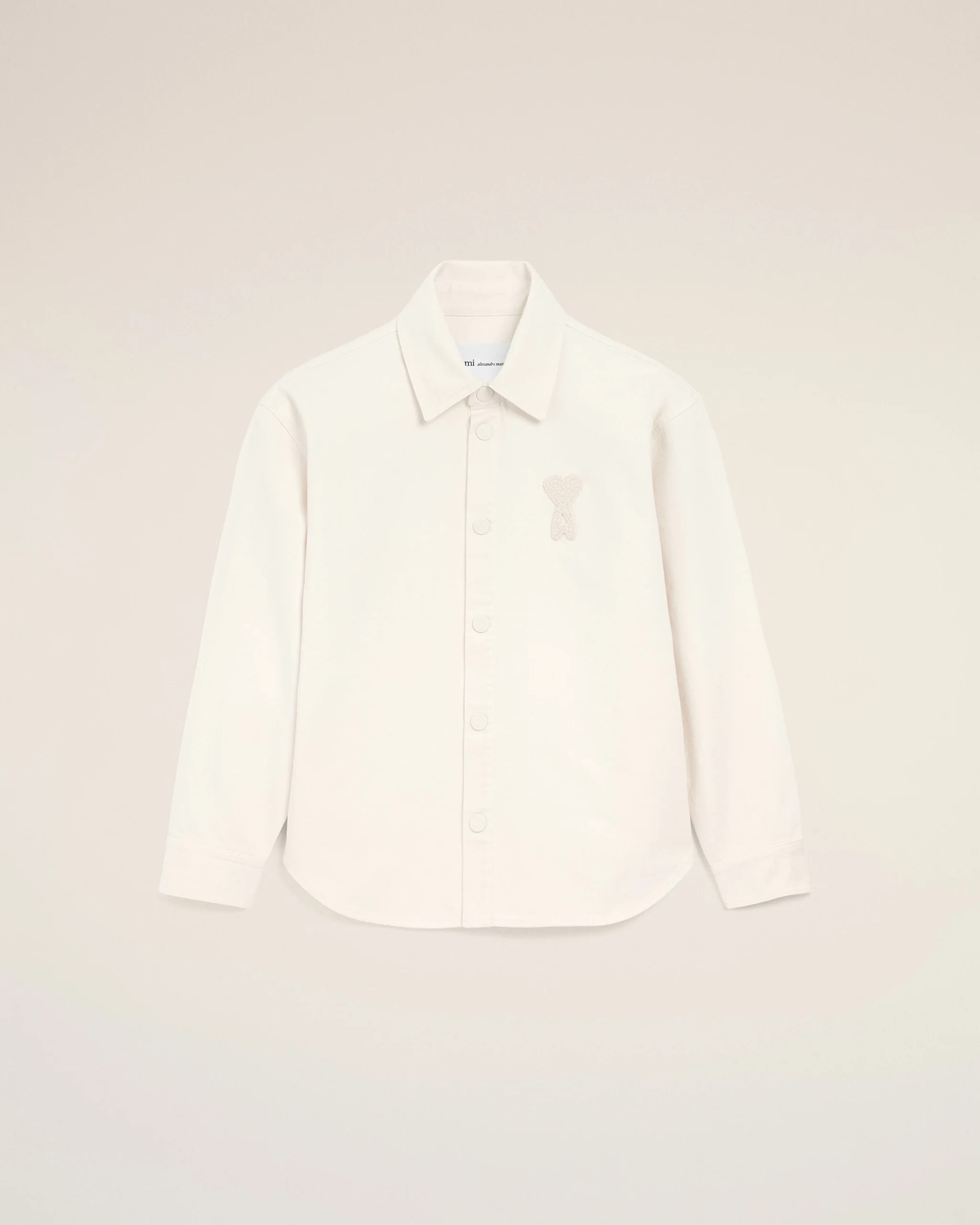 White button-down shirt with a small bear embroidery on the left chest, displayed against a pale beige background.