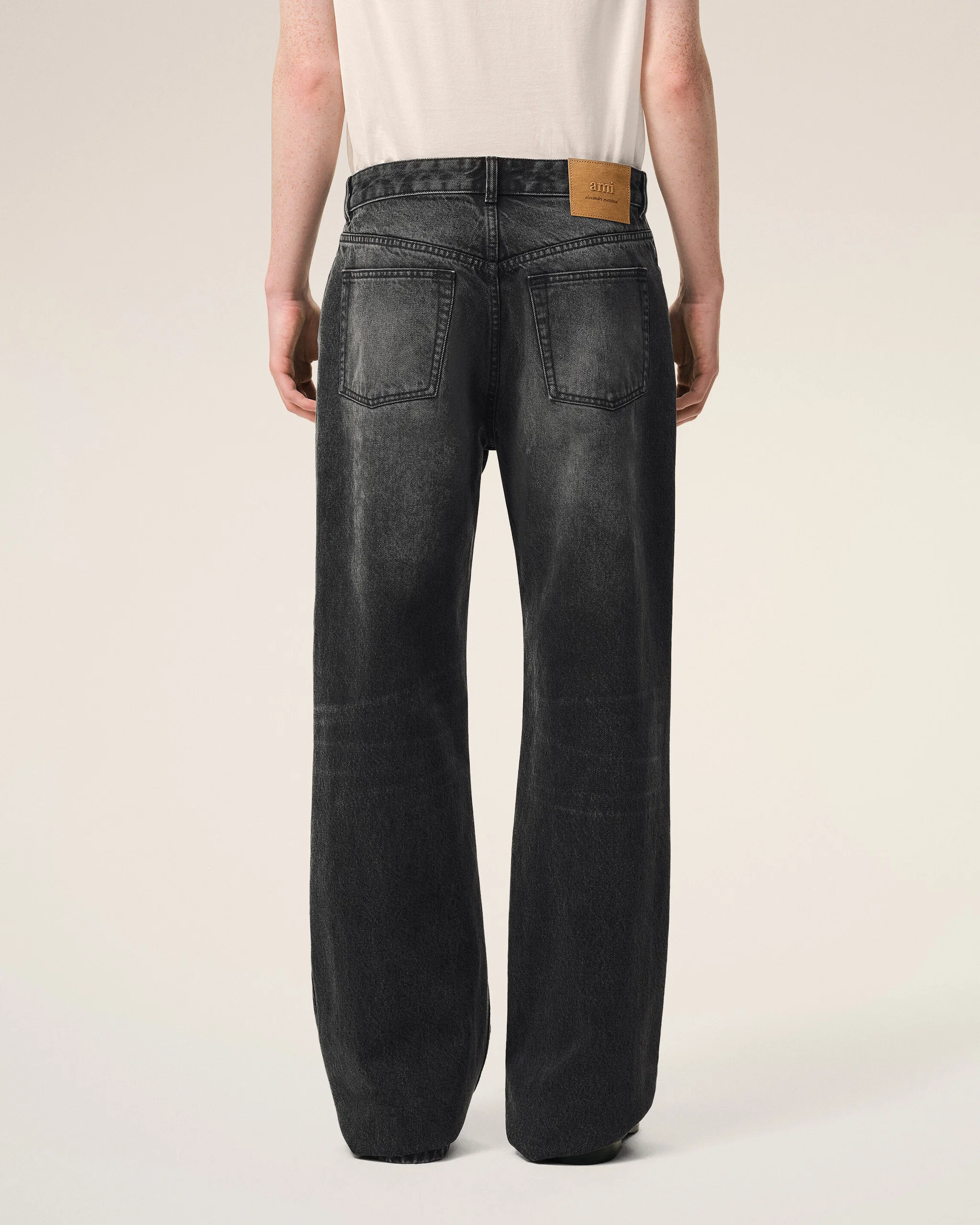 Back view of a person wearing dark wash jeans with two back pockets and a tan leather brand patch at the waistband on the right side.
