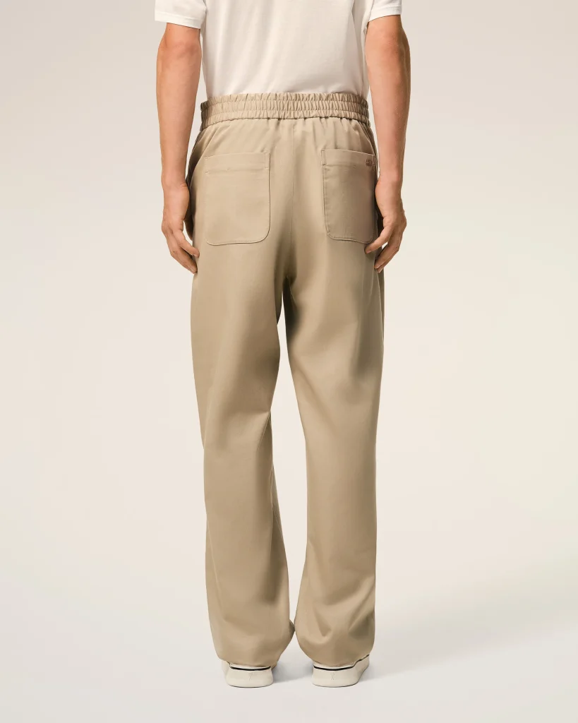 Back view of a person wearing beige elastic-waist pants with two back patch pockets and white sneakers, facing away.