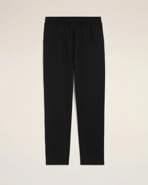 Black jogger pants with an elastic waistband and drawstring laid flat on a beige background, cropped view from the waist down to mid-thighs