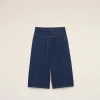 Top-half view of dark blue denim trousers with orange stitching laid flat on a light beige background