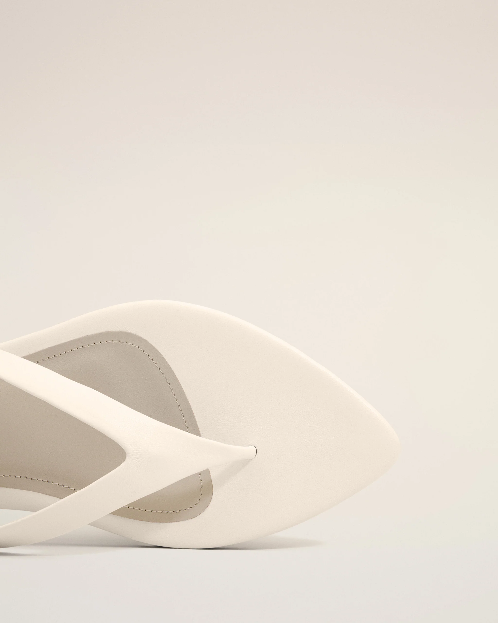 White sandal close-up showing leather straps and stitching on a pale background.