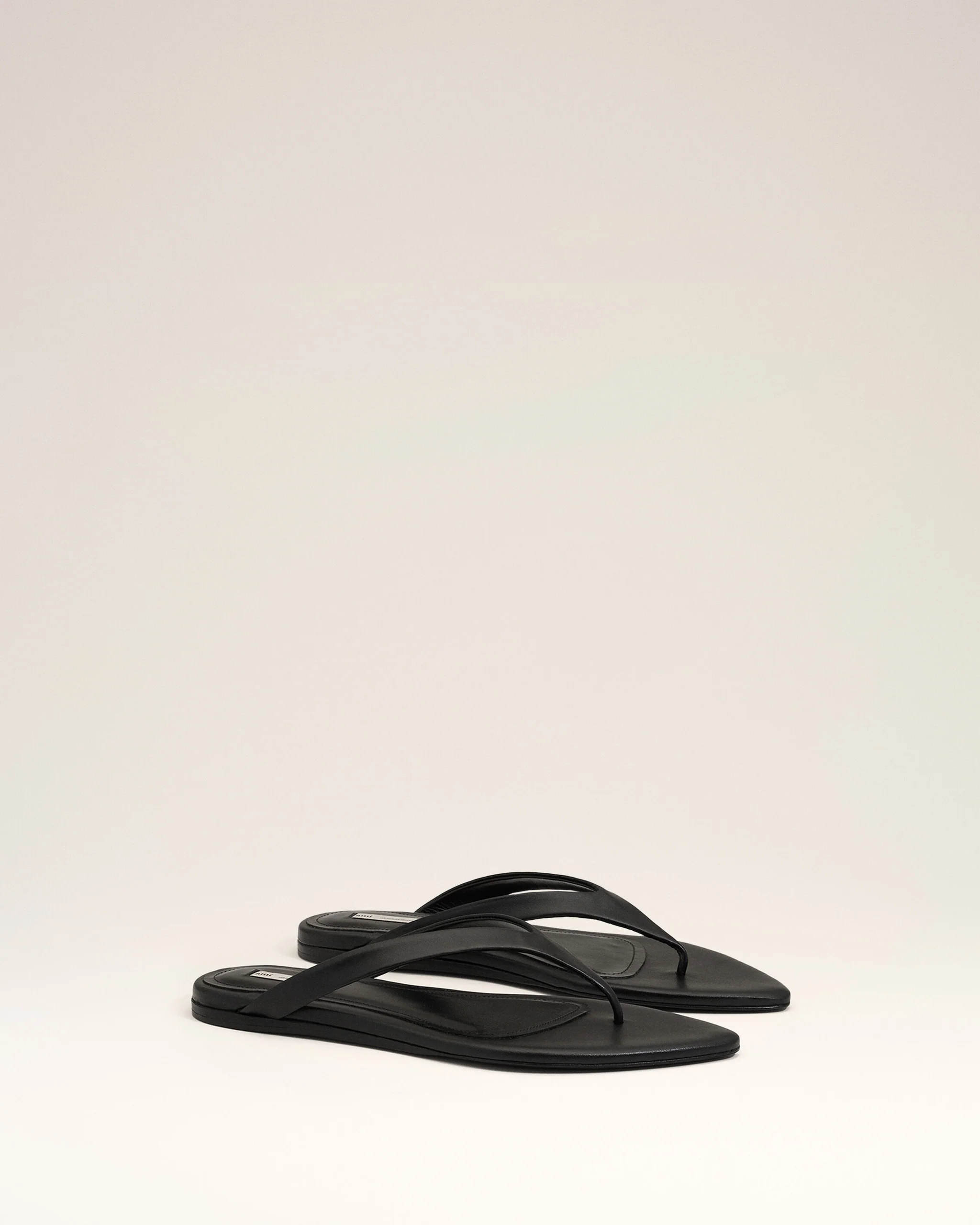 Pair of black flip-flop sandals with thin straps lying on a white surface.