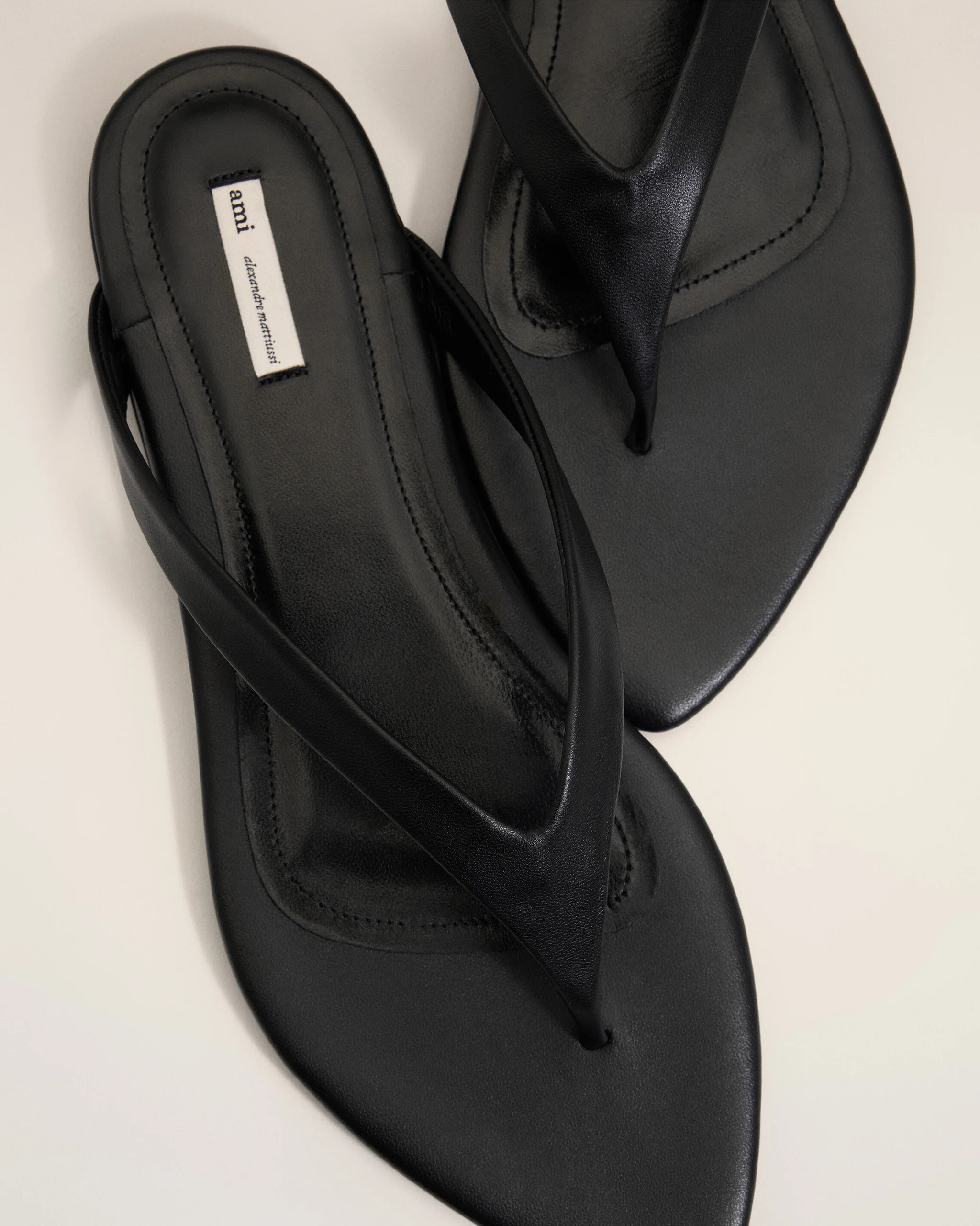 Black leather sandals with multiple crisscross straps and a small white fabric label on the insole reading 'ami' (brand tag).