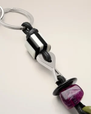 Close-up of a silver keyring with a black braided cord and purple marbled bead on a pale background, showing a metallic clasp.