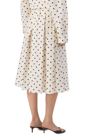 Beige polka-dot midi dress with a pleated skirt, shown with black heeled sandals from the knee down.