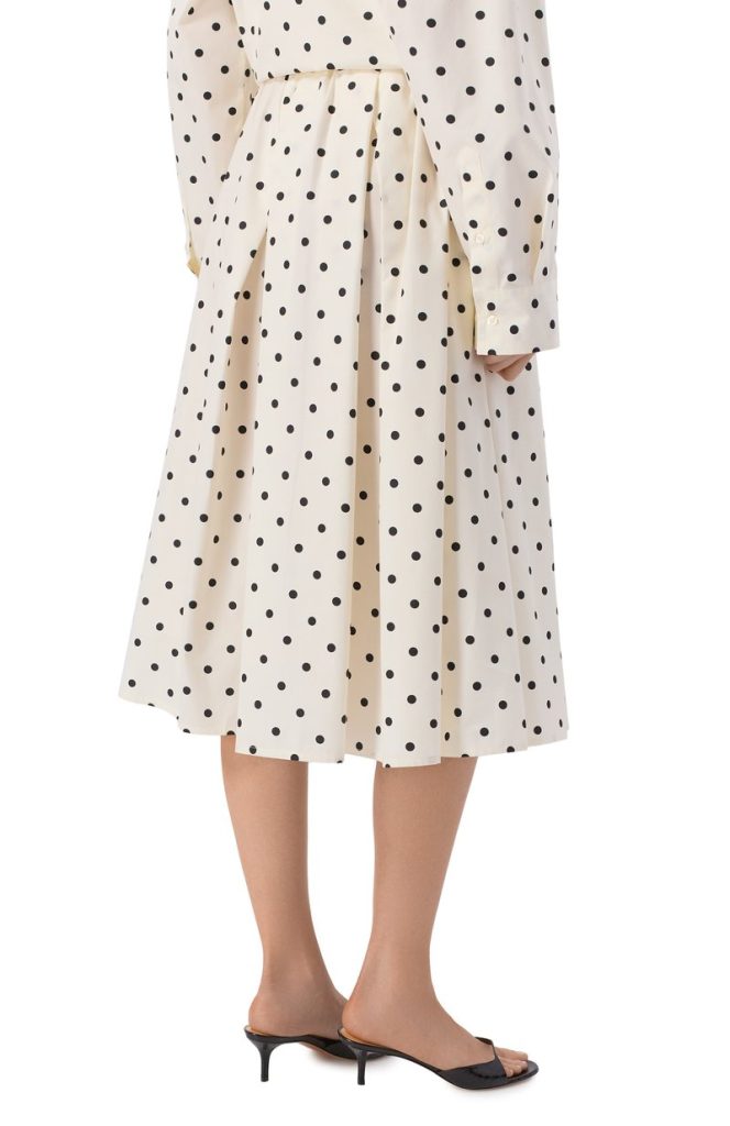 Beige polka-dot midi dress with a pleated skirt, shown with black heeled sandals from the knee down.