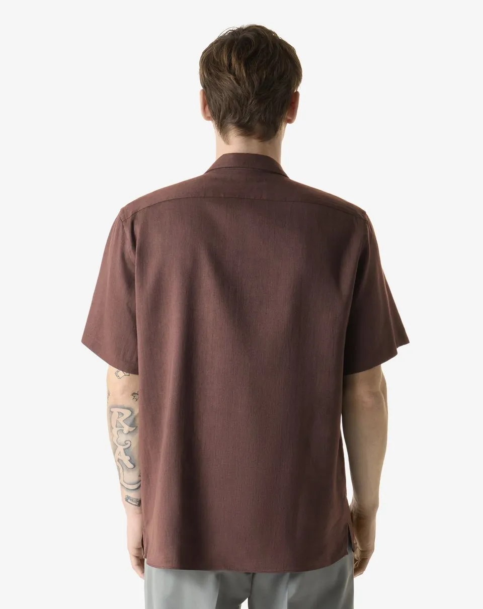 Man shown from behind wearing a brown short-sleeve shirt; tattoos visible on the left forearm.