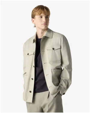 Young man wearing a light beige jacket over a black shirt, with hands in pockets, looking to the right, on a white background.