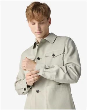 Young man in a light beige trench coat adjusting the cuff on his sleeve.