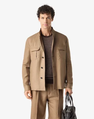 Man wearing a tan suit jacket over a brown striped sweater, holding a black bag visible at his side.