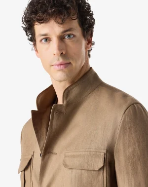 Close-up portrait of a man with curly brown hair wearing a tan coat, looking at the camera against a light background.