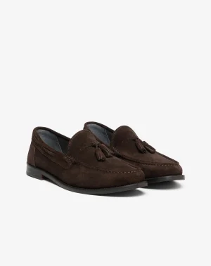 Brown suede loafers photographed from a low angle on a white background, showing the front and side details like tassels and stitching.