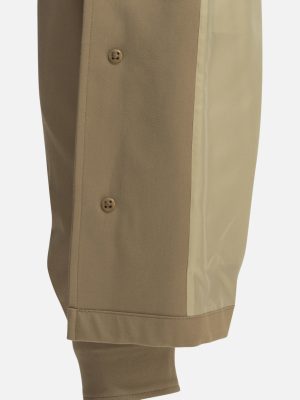 Close-up of a tan pant leg with a lighter beige side panel, small brown buttons, and a folded hem.