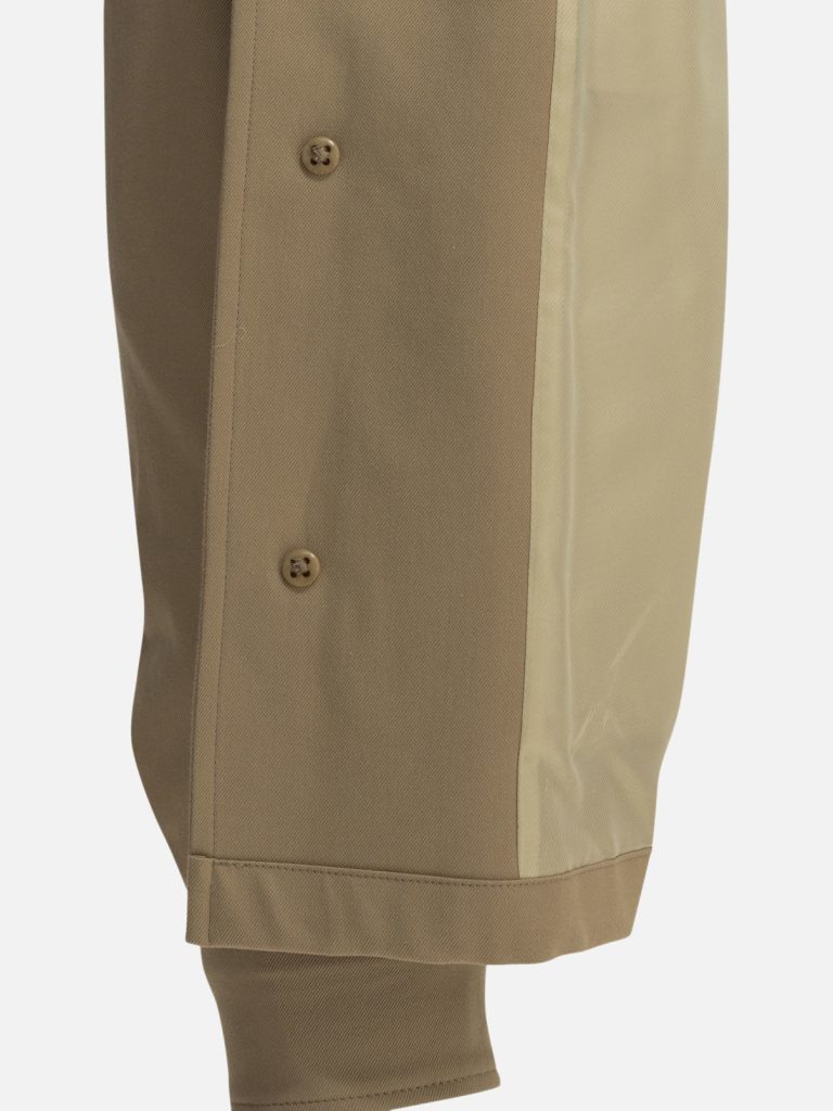 Close-up of a tan pant leg with a lighter beige side panel, small brown buttons, and a folded hem.