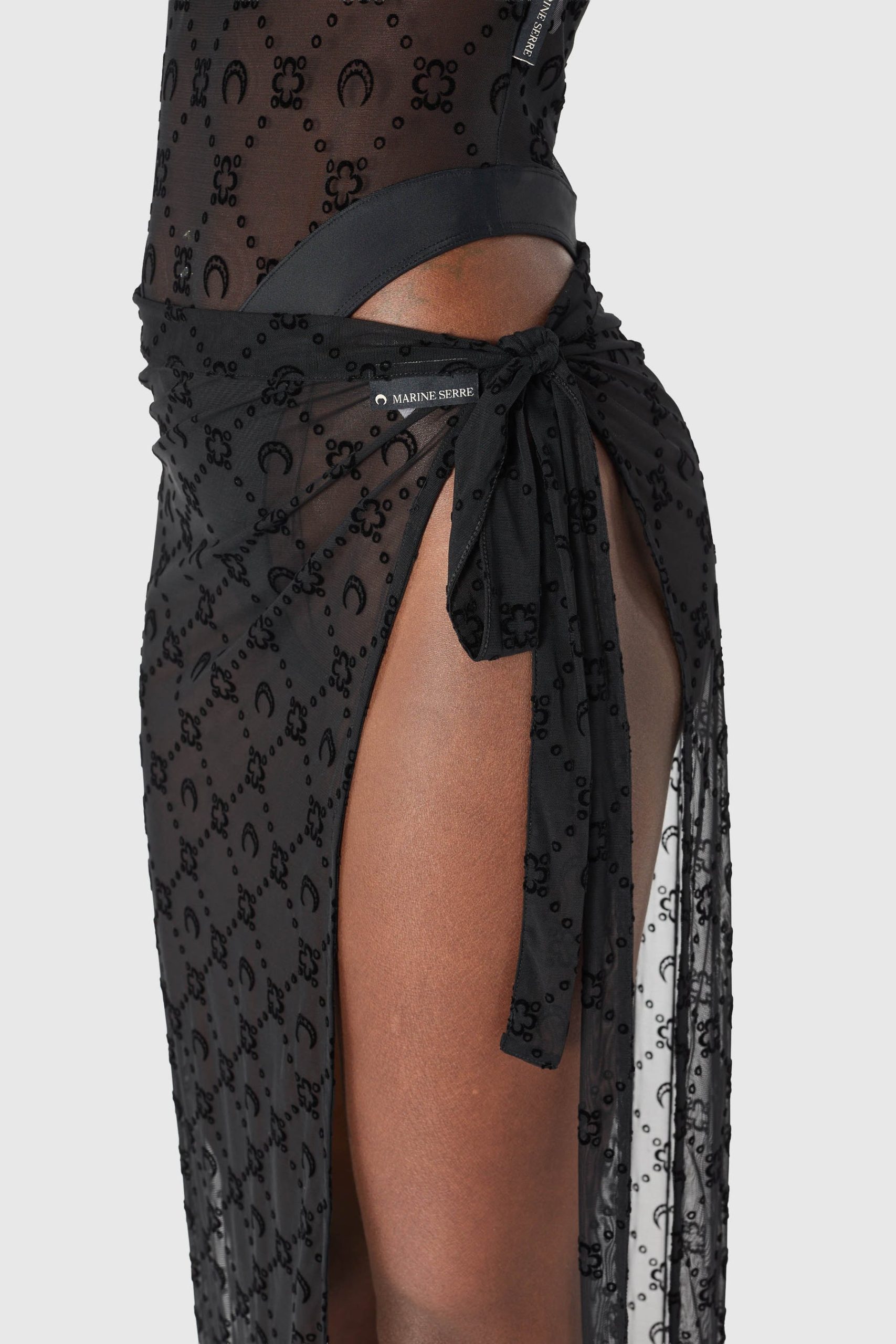 Close-up of sheer black fabric with a repeating pattern and a tied waist, showing a Marine Serre label.