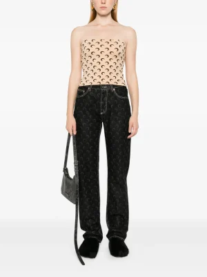 Model in a strapless beige top with a crescent pattern and black patterned wide-leg jeans, holding a gray shoulder bag.