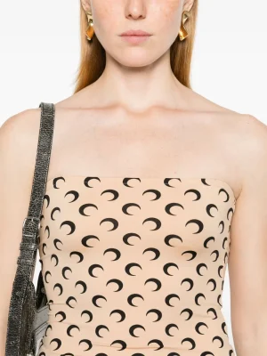 Model in a strapless beige top with a black crescent pattern, gold earrings, and a textured gray bag strap over her shoulder.