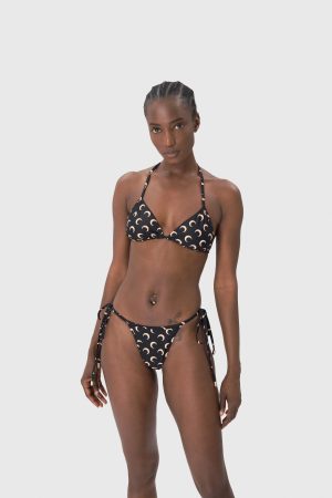 Black woman in a crescent-print bikini top and bottom, standing against a light gray studio background, facing camera.