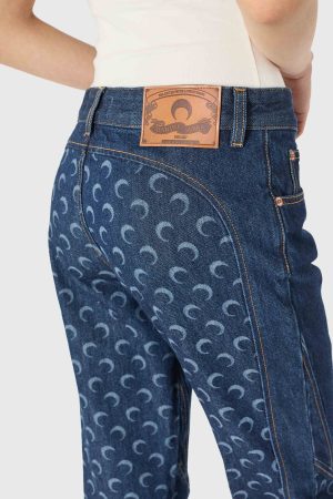 Back view of dark blue denim jeans with a brown leather patch at the waistband and a repeating crescent pattern on the fabric