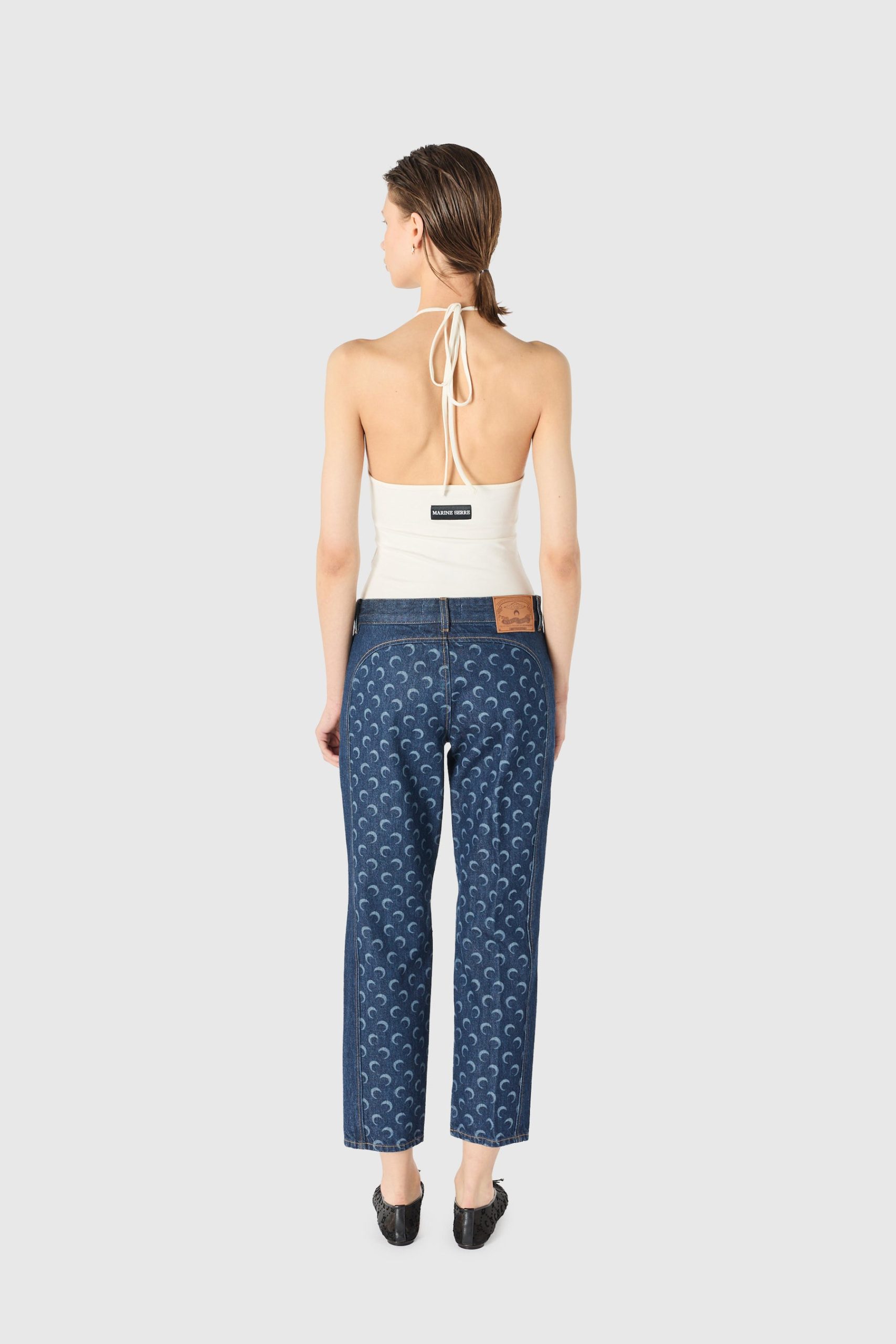 Back view of a woman wearing a white halter top and blue patterned jeans, hair in a low ponytail.