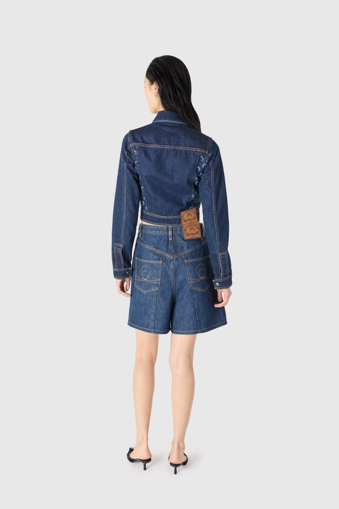Back view of a person wearing a denim jacket and matching high-waisted shorts, facing away.