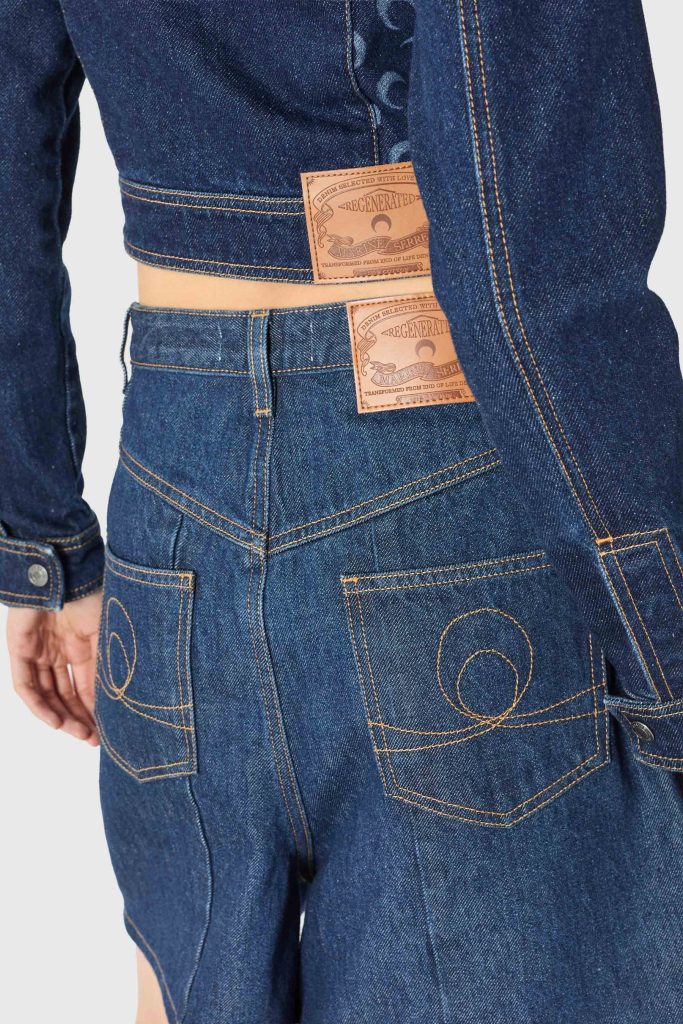 Close-up of a blue denim jacket and jeans with brown leather patches on the back, showing contrast orange stitching.
