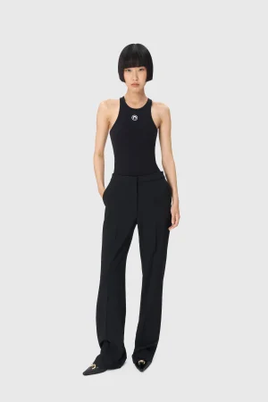 Model wearing a black sleeveless top and matching black wide-leg pants stands against a light gray background, facing the camera with a neutral expression.