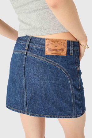 Back view of a person wearing a dark blue denim skirt with a brown leather patch at the waistband and a gray top.