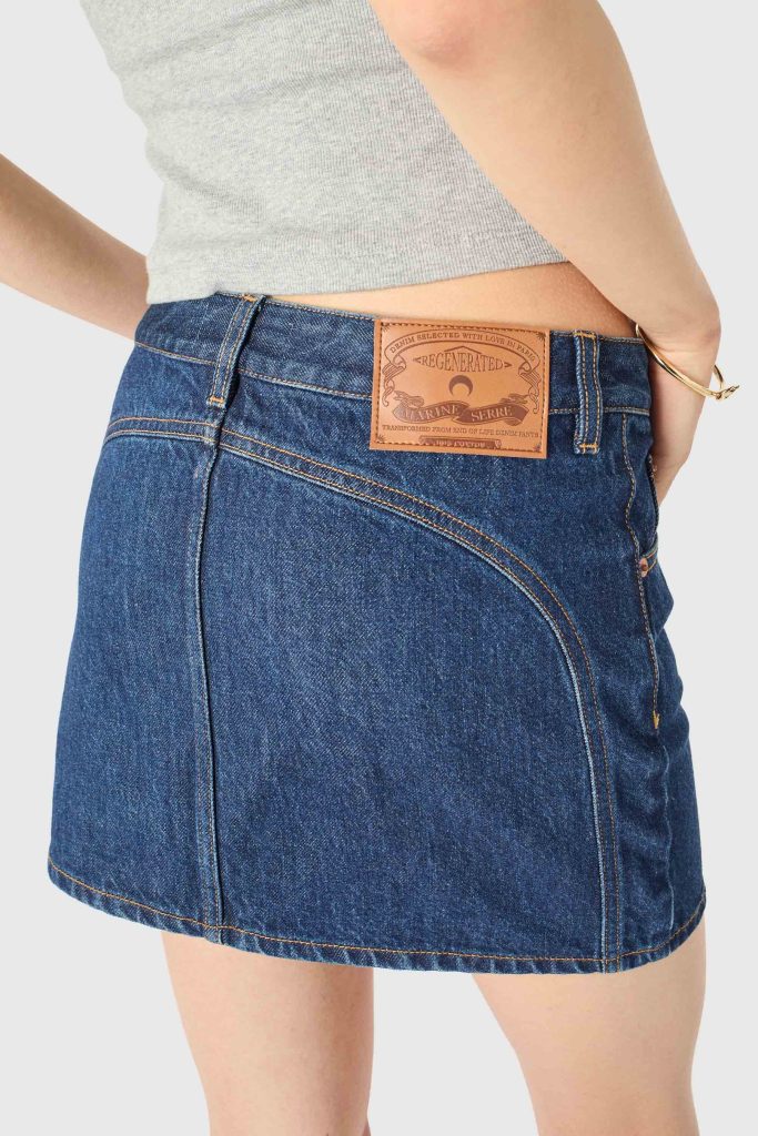 Back view of a person wearing a dark blue denim skirt with a brown leather patch at the waistband and a gray top.