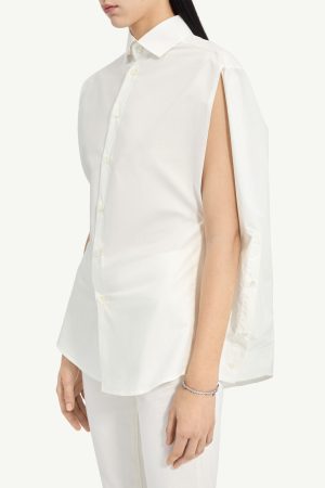 Side view of a white button-down shirt featuring a cape-like sleeve with an open shoulder slit, worn with white pants and a bracelet.